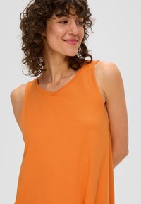 Oranje mouwloze top met een v-hals ontwerp, gemaakt van zachte stof, met een losse pasvorm en een gladde textuur, die de halslijn accentueert.