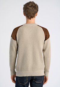 Beige neulepaita, jossa on ribbikuviointi, ruskeat mokkaolkapäät ja pyöreä kaula-aukko. Suunniteltu istuvaksi, jossa on pitkät hihat.