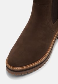 Botte Chelsea en cuir marron avec panneau latéral élastique, couture détaillée et semelle épaisse crantée sur fond clair.
