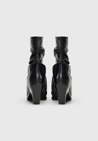 Bottes ankle en cuir noir avec un design affaissé, bout pointu et talons blocs de 4 cm. Présente des accents de rivets dorés sur la tige.