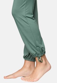 Pantaloni jogger verzi din bumbac, cu manșete elastice și șnururi la glezne, care prezintă o textură fină și un design ajustat pe picior.