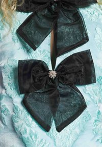 Tecido de cetim azul claro com bordados florais, apresentando dois grandes laços transparentes pretos com centros de strass.