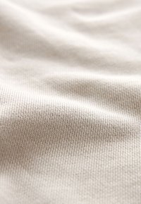 Tessuto beige testurizzato con un fine motivo a coste, che mette in mostra un materiale morbido e liscio con sottili variazioni di colore e profondità.