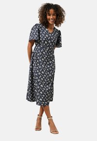 Vestido envolvente navy con estampado floral, mangas cortas con volantes, falda hasta los tobillos y print de flores blancas. Presenta un escote en V y bolsillos laterales.