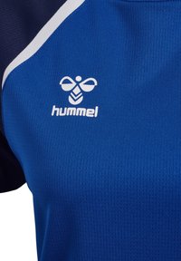 Blue and navy sports jersey with white chevron bee logo and "hummel" text on chest, featuring breathable mesh fabric and white diagonal stripe.