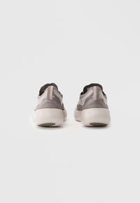 Grå strikkede sneakers med en tekstureret overflade, der har en beige sål og mørke detaljer. Bagfra ses en pull-tab på hælen for nem påføring.