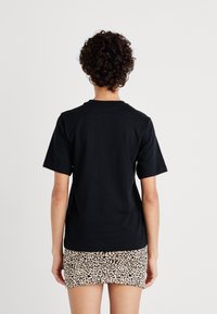 Černé bavlněné tričko s krátkým rukávem, kulatým výstřihem a volným střihem, kombinované s mini sukní s leopardím potiskem. Pohled ze zad.