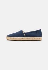 Sininen kangas-espadrille, jossa on juuttiköysisole, suljettu kärki ja joustavat sivuinsertit helppoa pukemista varten. Merkkilogo sivulla.