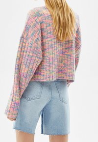Pull court en tricot multicolore présentant des manches longues, une texture côtelée et un motif à carreaux vibrant, assorti à un short en denim taille haute.