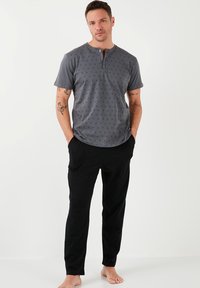 Camisa gris de manga corta con un sutil patrón triangular y una tapeta de tres botones, combinada con pantalones negros con bolsillos laterales.