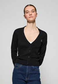 Cardigan en maille noire avec un décolleté en V, fermeture à boutons et ourlet côtelé. Présente un petit logo brodé sur le côté gauche. Texture lisse.