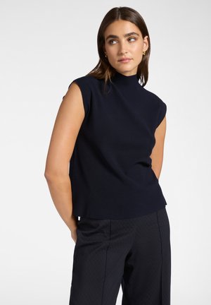 Top senza maniche blu navy con collo alto, in tessuto testurizzato e vestibilità dritta. Abbinato a pantaloni scuri a fantasia.