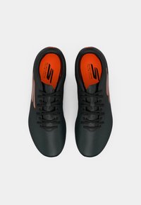 Black athletic shoes with synthetic upper, orange insoles, and black laces. Features include perforations and a sleek, rounded design.
