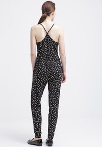 Mono negro con un patrón floral blanco, con tirantes finos y un diseño ajustado que se estrecha en los tobillos, hecho de una tela ligera.