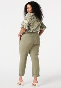 Blouse à motif paisley avec des manches à volants, associée à un pantalon de jogging tapered vert olive avec une taille élastique et des poches arrière.
