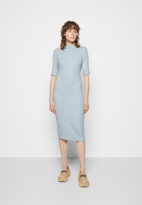 Vestido midi azul claro com mangas curtas, gola alta e textura suave, combinado com sapatos de plataforma bege com detalhe em corrente.