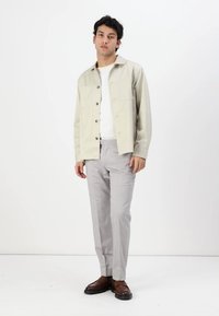 Light beige button-up jacket over a white t-shirt, paired with light gray trousers and brown shoes. Simple design and neutral colors.