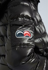 Schwarzer, glänzender gepolsterter Jackenärmel mit einer Tasche, die ein blaues und rotes Berglogo-Patch und einen Druckknopfverschluss aufweist.