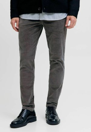Pantaloni in velluto a coste grigio scuro, design slim-fit, caratterizzati da una texture a coste verticali. Abbinati a scarpe eleganti in pelle nera.