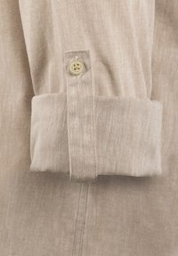 Puño de camisa de lino beige con un cierre de un solo botón, doblado de manera ordenada con una textura suave y un sutil detalle de costura a lo largo de la costura.