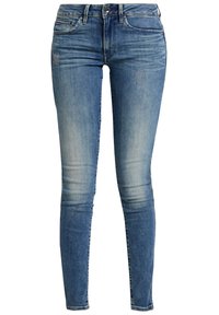 Jeans skinny di colore blu in denim lavato medio. Presentano un leggero sbiadimento, dettagli di cucitura e un classico design a 5 tasche.