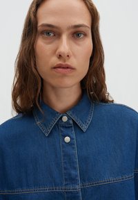 Blauw denim overhemd met een puntige kraag en drukknoopsluiting, voorzien van opvallende stiksels en een ontspannen pasvorm. Soepele textuur, casual stijl.
