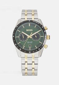 Orologio dual-time con quadrante verde, cinturino in acciaio inossidabile oro e argento, lunetta tachimetrica nera e sub-quadranti cronografici. Resistente all'acqua fino a 5 bar.