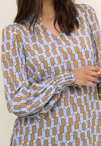 Halenka s dlouhým rukávem s geometrickým vzorem v hnědé, světle modré a krémové barvě. Látka má hladkou strukturu s nařasenými manžetami.