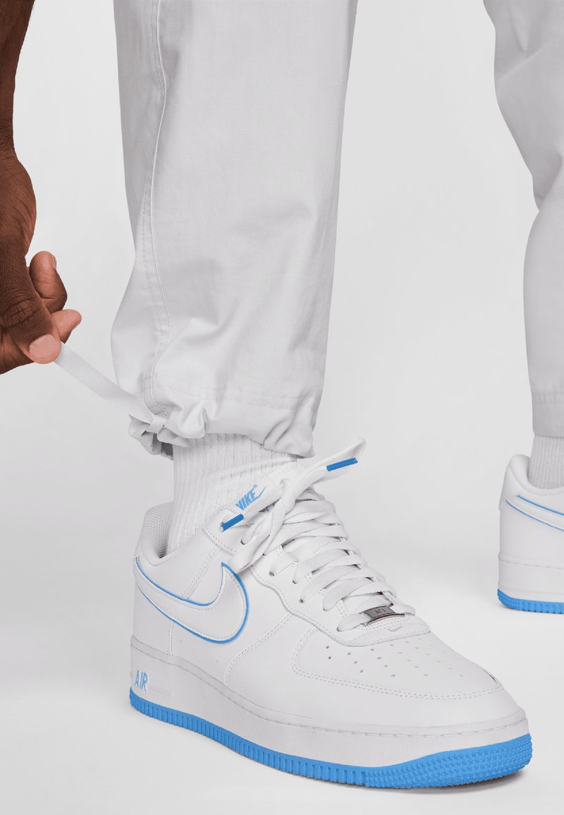 Białe sneakersy Nike Air Force 1 z niebieskimi akcentami, z gładką skórzaną cholewką, perforowanymi palcami i teksturowanymi gumowymi podeszwami.