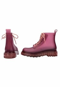 Botas de tobillo moradas translúcidas con una suela gruesa transparente. Presenta un material similar al cuero, punta redonda y cordones en contraste.