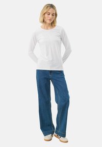 White long-sleeve shirt paired with blue wide-leg jeans. Shirt has a crew neck; jeans feature visible stitching and relaxed fit.