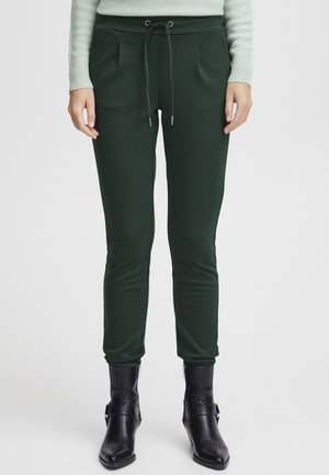 Green, fitted jogger pants with a drawstring waist, pleats, and soft texture, paired with black zippered ankle boots.