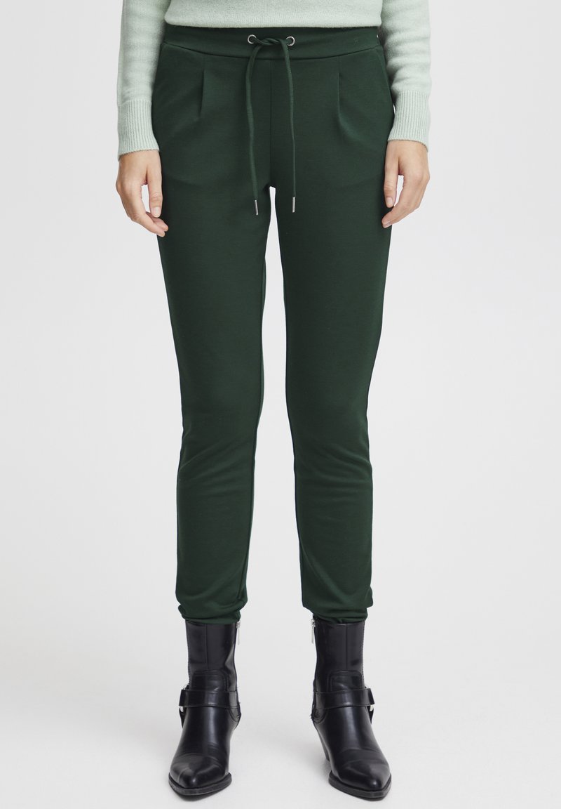 Green, fitted jogger pants with a drawstring waist, pleats, and soft texture, paired with black zippered ankle boots.