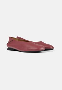 Bailarinas de cuero rojo con tacón bajo, puntera cerrada y un ligero corte en el tobillo. Textura suave con suelas de goma negra. Diseño minimalista.