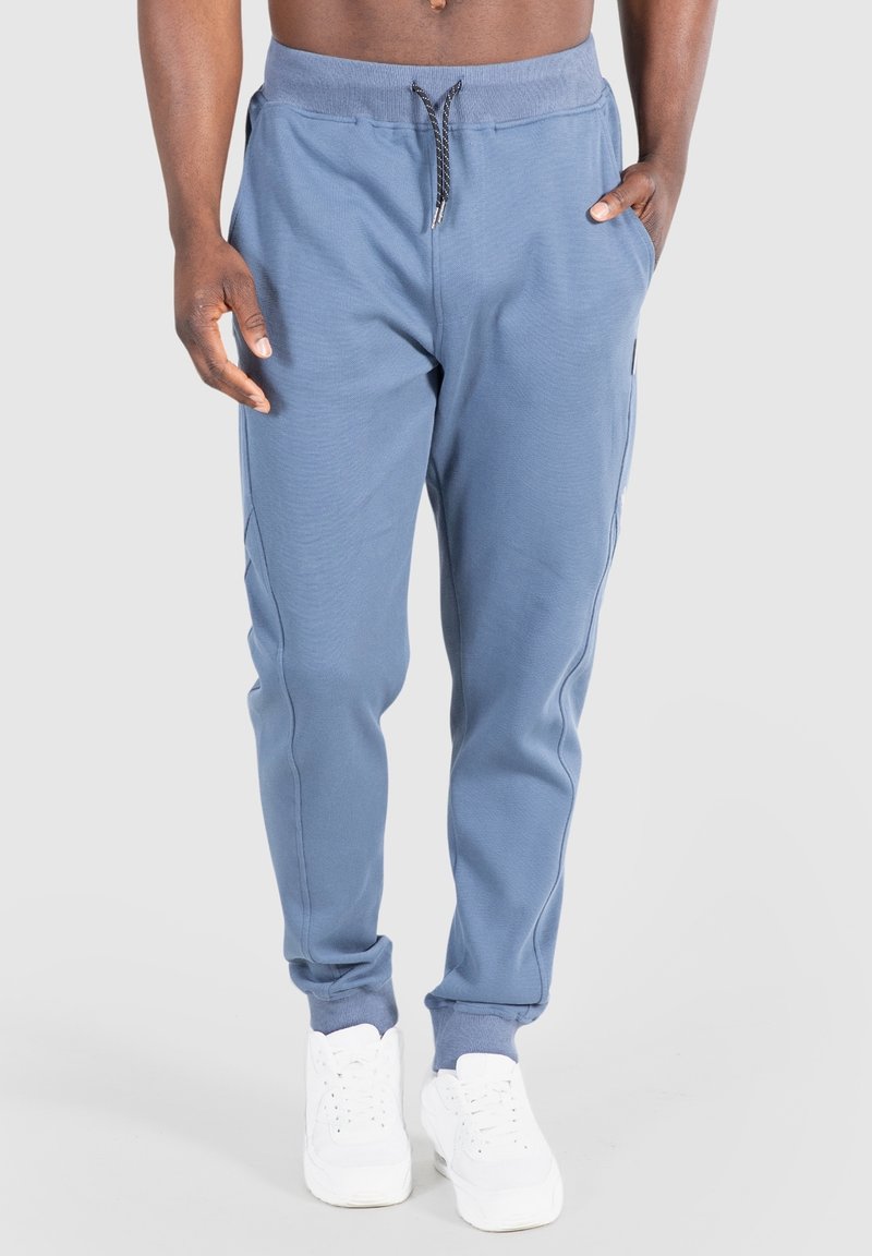 Modré tepláky z měkké látky, vybavené pasem se šňůrkou a žebrovanými manžetami. Součástí jsou i boční kapsy pro uložení věcí.