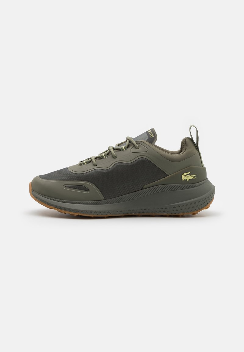 Basket basse vert olive et gris foncé avec semelle texturée, lacets à l’avant, languette au talon, et logo crocodile Lacoste jaune sur le côté.