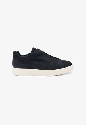 Sneaker slip-on in suede nera con suola in gomma bianca, caratterizzata da cuciture blu e un design snodato. Senza lacci visibili.