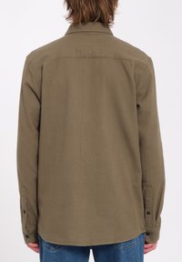Olivengrøn skjorte med knapper, lange ærmer med knapmanchetter, blødt stof, lige rygsømme, buet kant, båret over blå jeans.