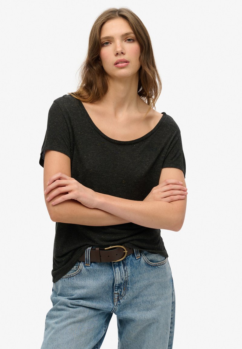 Camiseta negra de manga corta con un escote amplio, hecha de material suave. Metida dentro de unos pantalones vaqueros de corte ancho y color azul claro, combinada con un cinturón marrón.