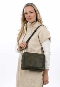 Borsa in pelle verde oliva con un accento intrecciato, hardware silver e tracolla regolabile, tenuta da una donna con un cappotto in pile crema.