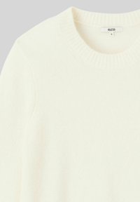 Pull en maille couleur crème avec un col rond côtelé, texture douce et léger éclat. L'étiquette indique "BZB" et taille "S."
