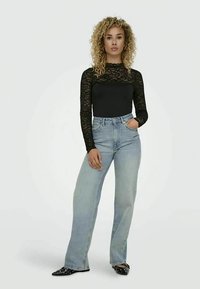 Top de renda preta de mangas longas combinado com jeans de perna reta azul claro. Sapatos pretos de bico fino com embellishments prateados.
