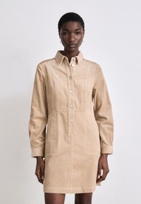 Beige Kordkleid mit Kragen, Knopfleiste, langen Ärmeln und zwei vorderen Taschen mit gerippter Textur.