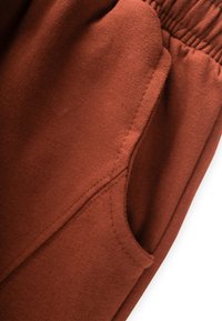 Brauner Fleece-Stoff mit glatter Textur; verfügt über einen elastischen Bund und eine Seitenasche für zusätzliche Funktionalität.