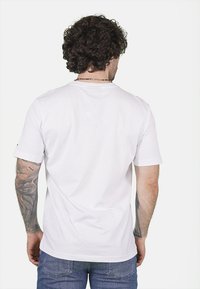 T-shirt bianco in cotone con maniche corte e vestibilità rilassata. Presenta un colletto rotondo e un dettaglio di cucitura minimale sulla parte posteriore.