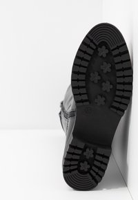 Botte noire avec une semelle en caoutchouc texturé arborant des motifs floraux, fermeture éclair sur le côté, et en matériau synthétique. Taille indiquée comme 37 au niveau de la semelle.