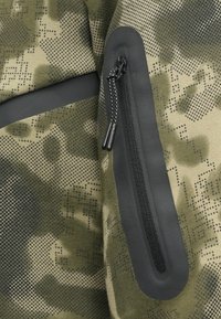 Kamuflāžas audums ar teksturētu zaļi melnu rakstu. Aprīkots ar melnu rāvējslēdzēju un gludām, noapaļotām akcentiem, kas nodrošina izturību.