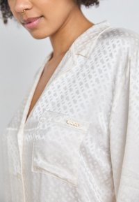 Blusa bianca con un sottile motivo geometrico, finitura satinata e una tasca con un accento del logo dorato "BOSS".