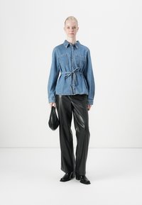 Denim shirt met een taille met riem, lange mouwen en twee voorzakken, gecombineerd met zwart leren broeken met hoge taille en enkellaarsjes.