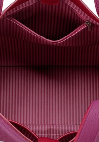 Inside of a pink handbag featuring smooth leather material, with a striped fabric lining in shades of pink and a small zippered pocket.